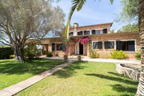 A stone house with a garden, a large tree, and a clear sky. - Es Molí: Views, Mallorca Essence and Private pool (Santa Eugènia)