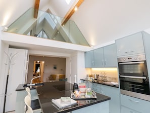 A modern kitchen with a central island, a built-in oven, and a glass staircase. - Little Mornington (Malvern)