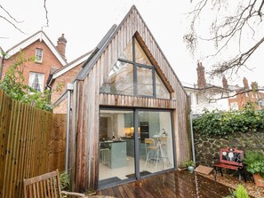 A modern house with a sloped roof, a large glass door, and a wooden deck. - Little Mornington (Malvern)