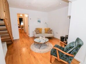 Una sala de estar con sofá, mesa de centro y un sillón estampado. Se ve una escalera a la izquierda.