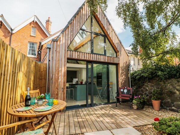 A modern house with a wooden exterior, a glass conservatory, and a patio with outdoor furniture. - Little Mornington (Malvern)