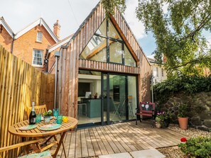 A modern house with a wooden exterior, a glass conservatory, and a patio with outdoor furniture. - Little Mornington (Malvern)