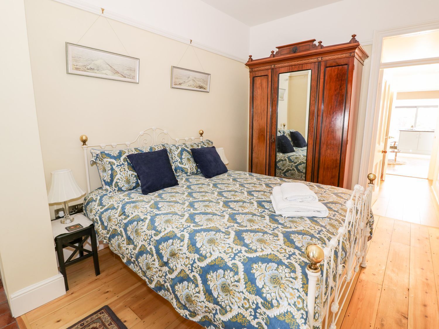 A bedroom with a bed, a nightstand, a mirror, and a wooden wardrobe.