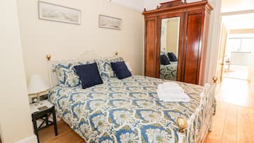 A bedroom with a bed, a nightstand, a mirror, and a wooden wardrobe.
