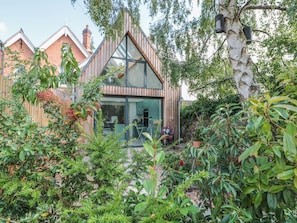 A modern house with a glass facade, surrounded by lush greenery and a large tree. - Little Mornington (Malvern)