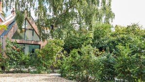 A modern building with a sloped roof, surrounded by dense greenery and a gravel path. - Little Mornington (Malvern)