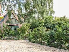 A modern building with a sloped roof, surrounded by dense greenery and a gravel path. - Little Mornington (Malvern)