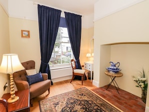 A cozy living room with a sofa, a lamp, a rug, and a window with curtains. - Little Mornington (Malvern)