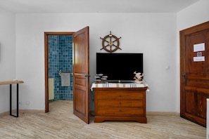 A room with a wooden dresser, a television, a wall-mounted ship's wheel, and a tiled wall.