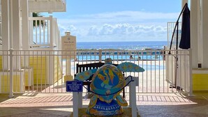 A covered area with a view of a beach and pool, featuring a turtle sculpture and a sign warning against climbing the turtle.