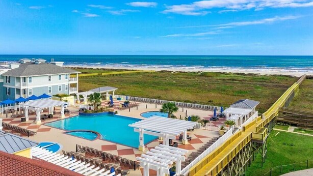 A pool area with a view of the ocean, a pier, and a building with a balcony.