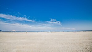 A wide, open beach with a clear sky and a few distant structures.
