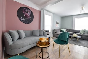 A modern living room with a grey sofa, a teal chair, and a round coffee table with gold accents. - The Smith - Renovated 4 Bedroom (Prince Edward)