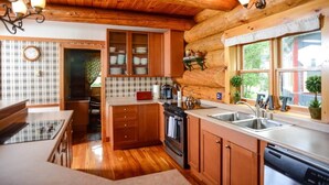 A wooden cabin interior with a kitchen featuring a stove, sink, and cabinets. - The Log House - Wellington - with Fast Wifi (Wellington)
