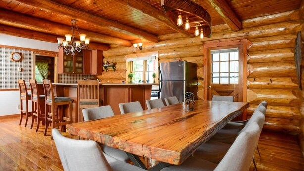 A log cabin interior with a wooden dining table, chairs, a kitchen area, and a chandelier. - The Log House - Wellington - with Fast Wifi (Wellington)