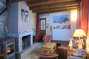 A cozy living room with a stone fireplace, wooden furniture, and a view of mountains through a window. - Chalet in Savoyard village (Les Belleville)