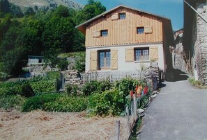 A two-story wooden building with shutters, a stone wall, and a pathway leading to it. - Chalet in Savoyard village (Les Belleville)