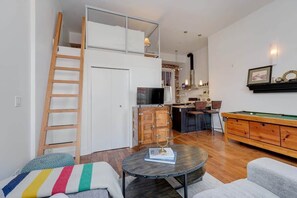 Un appartement de style industriel avec un lit en mezzanine, un coin repas, une table de billard et une cuisine.