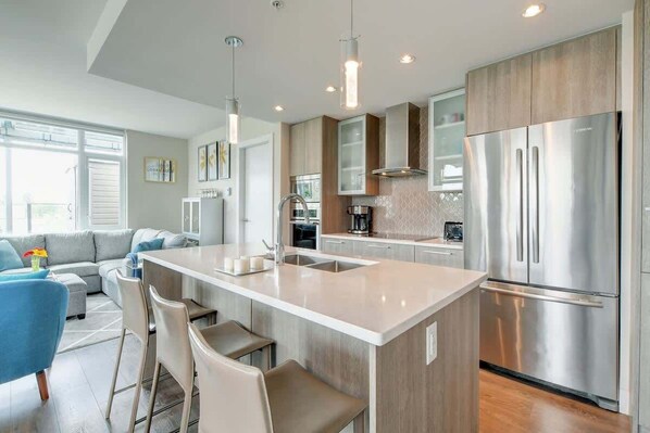 Una cocina moderna con una isla central, electrodomésticos de acero inoxidable y una zona de comedor con taburetes de bar.