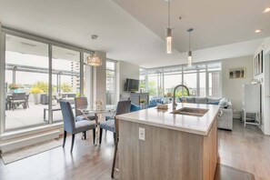 Una cocina moderna con una isla central, ventanas amplias y una zona de comedor con sillas y una mesa.