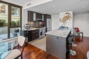A modern kitchen with dark cabinetry, a central island, and a dining area with a glass table and chairs.