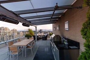 A rooftop patio with a table and chairs, a grill, and a sink.