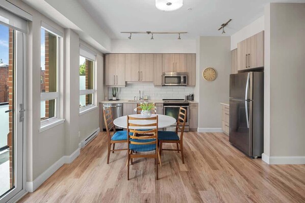A modern kitchen with a dining table, chairs, and stainless steel appliances. - Cozy Downtown Victoria Condo (Victoria)