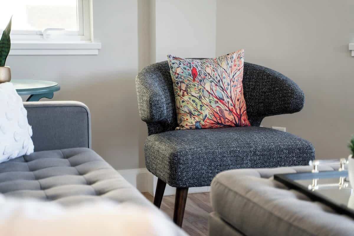 Ein modernes Wohnzimmer mit einem grauen Sessel, einer gepolsterten Couch und einem kleinen runden Tisch.