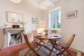 A dining area with a round wooden table, four wooden chairs, a fireplace, and framed artwork on the walls.