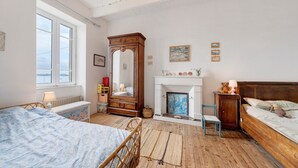 A bedroom with a bed, a dresser, a mirror, a fireplace, and a window.