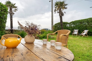 A wooden table with a yellow teapot, white cups, and a vase with dried plants.