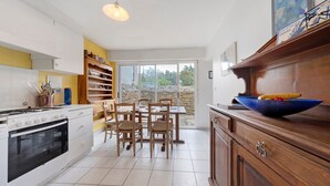Une cuisine avec des meubles blancs, une cuisinière, une table à manger avec des chaises et une grande fenêtre.