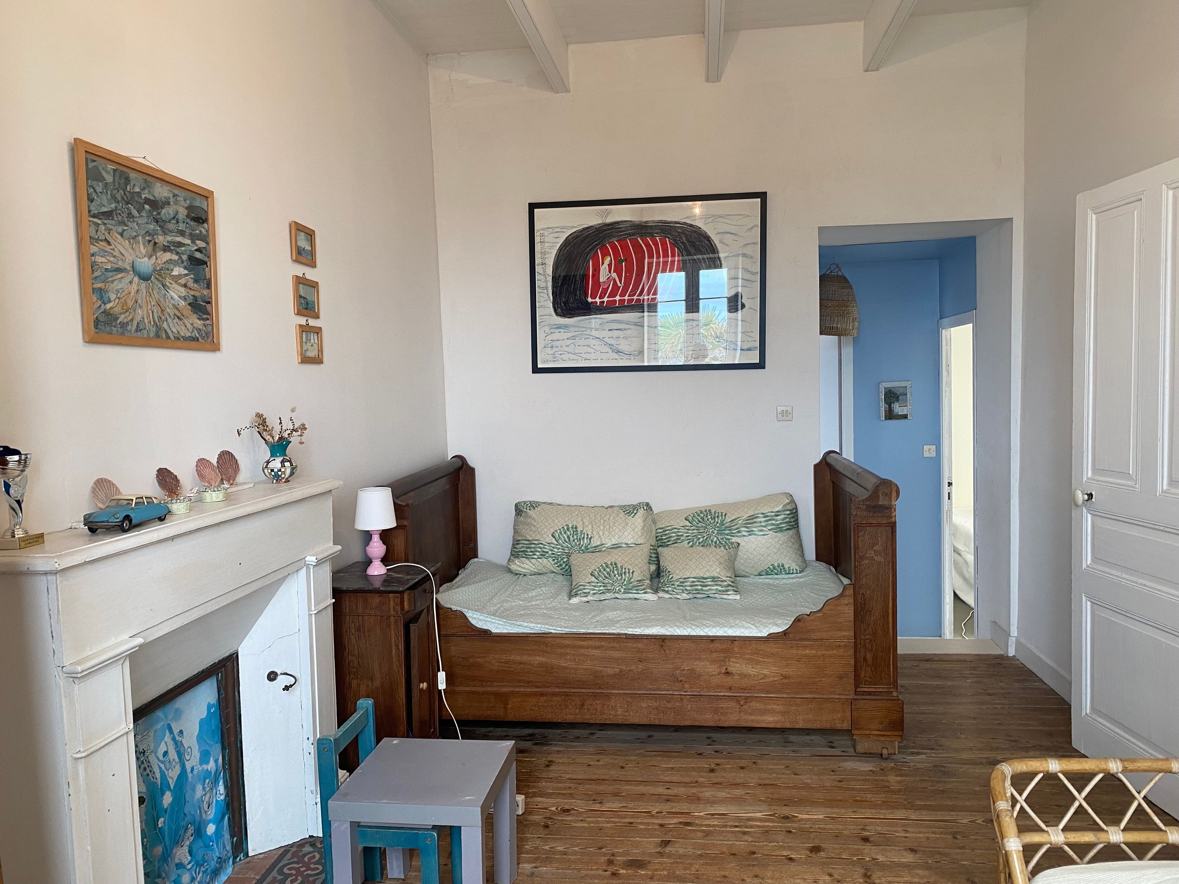 A cozy room with a wooden bed, a small table, a chair, a fireplace, and a wall with framed artwork.