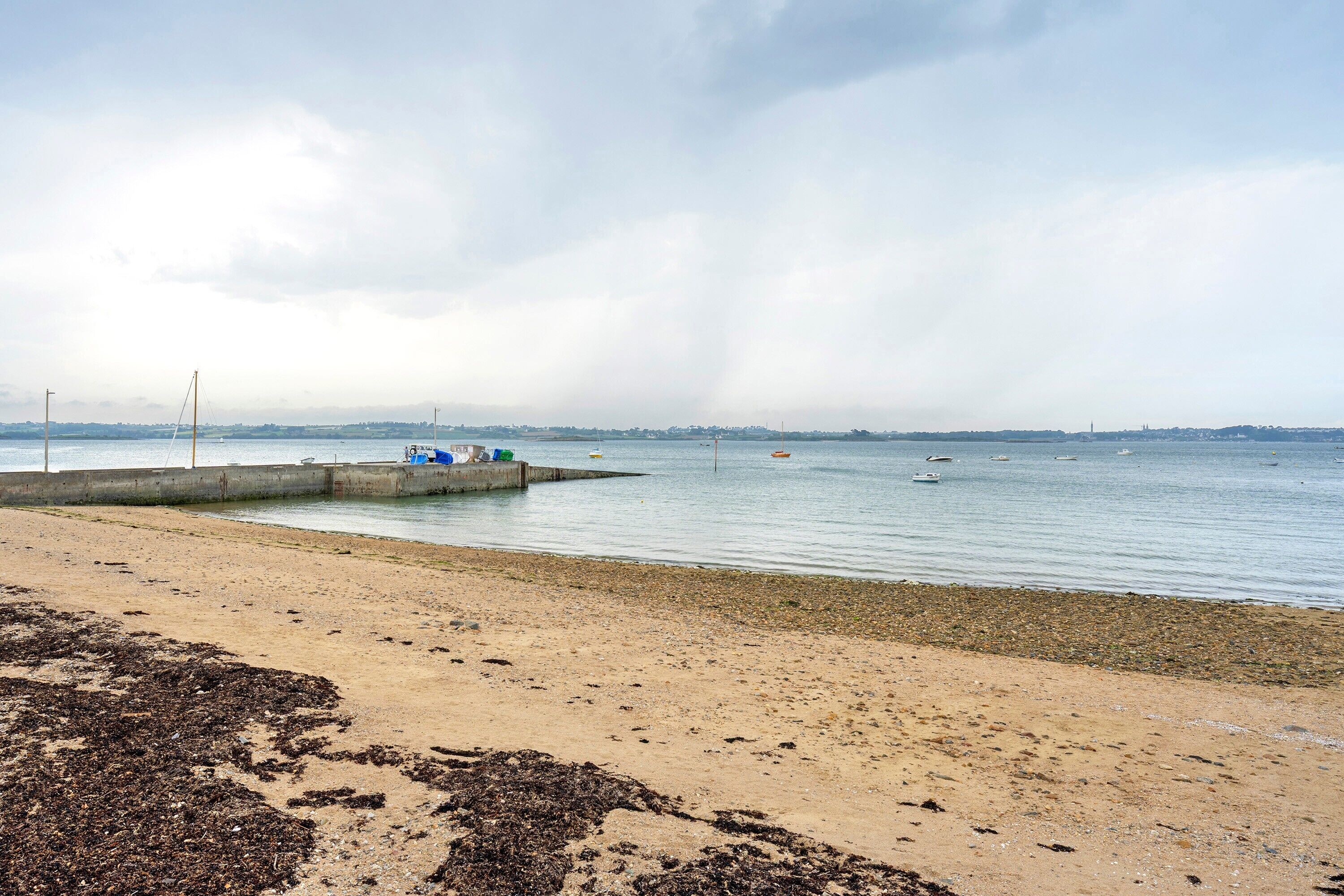 Une plage avec une jetée en béton, une eau calme et une vue lointaine sur les gratte-ciel de la ville.
