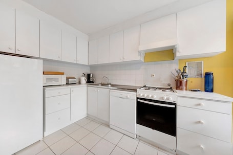 A modern kitchen with white cabinets, a dishwasher, a stove, and a microwave.. Fisherman’s House Facing the Sea with Ocean View and Direct Beach Access – Carantec, Baie de Morlaix