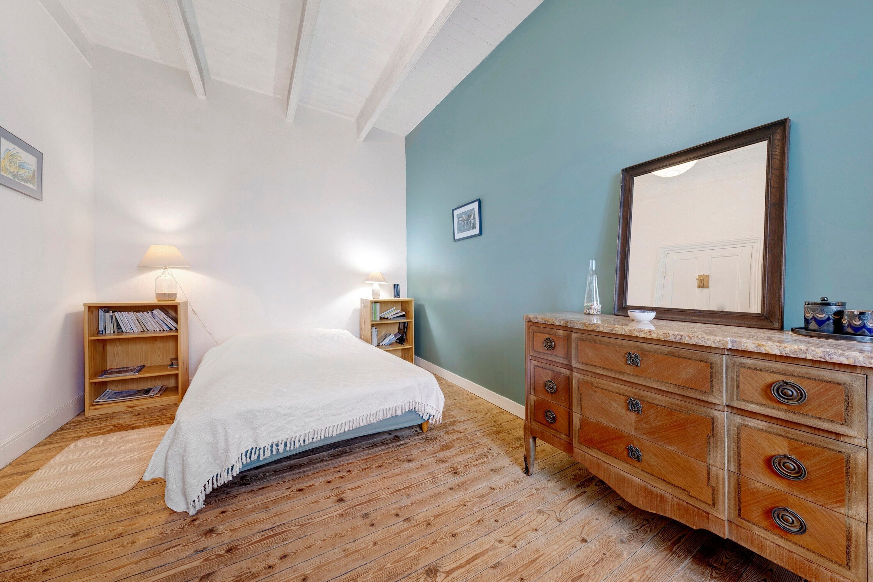 Une chambre à coucher comprenant un lit, une commode en bois, des tables de chevet et un grand miroir.