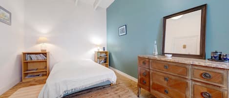 Une chambre à coucher comprenant un lit, une commode en bois, des tables de chevet et un grand miroir.