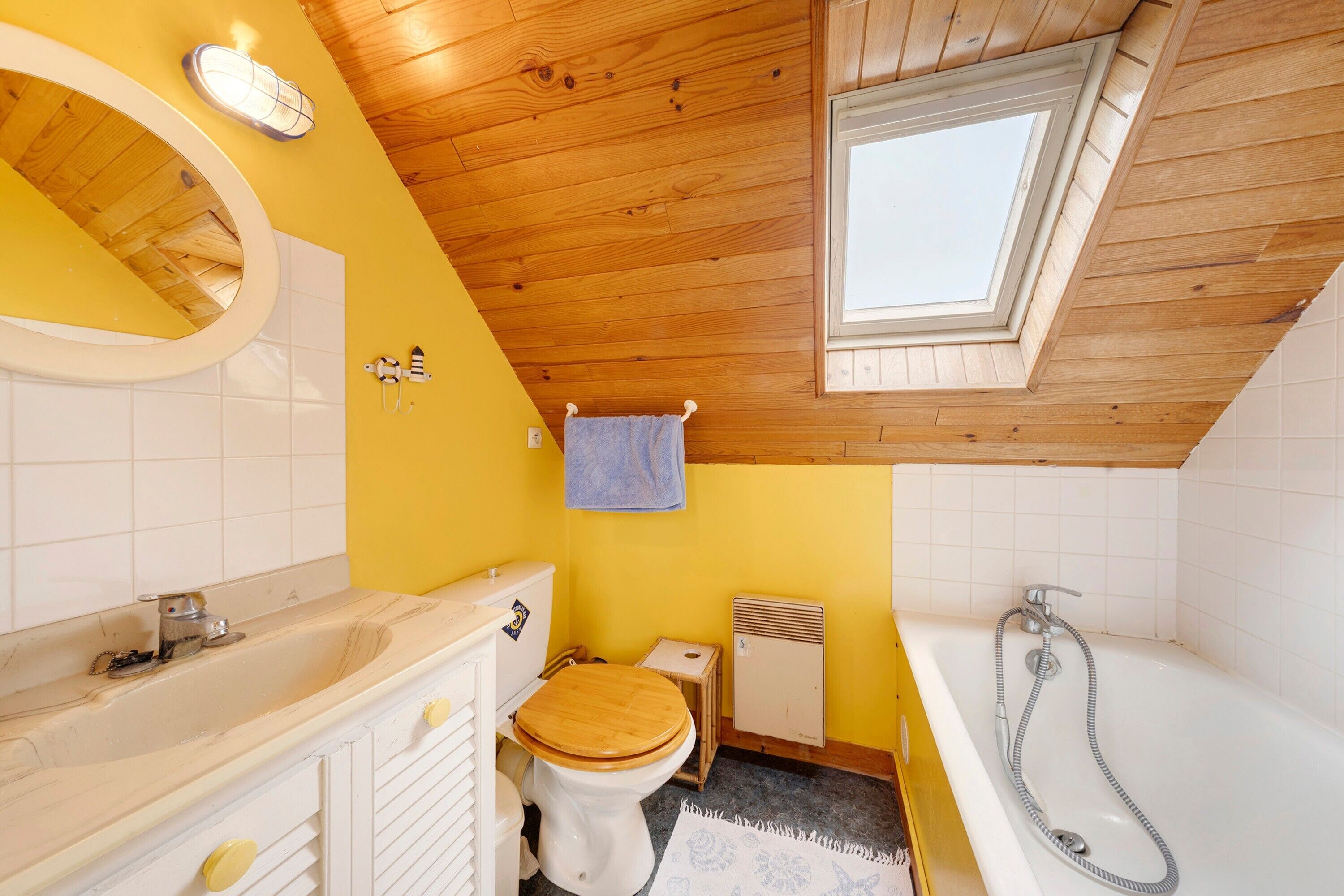 Une salle de bain avec un plafond en bois, un puits de lumière, des toilettes, une baignoire avec un pommeau de douche et un lavabo avec un miroir.