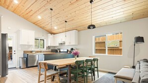 A modern kitchen with wooden ceiling, white cabinets, and a dining area with a wooden table and chairs. - 3bdr Modern Family House - Spa, Playroom, Walkable, Pet-friendly (Big Bear Lake)