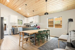Una cocina moderna con techo de madera, armarios blancos y un comedor con mesa y sillas de madera.