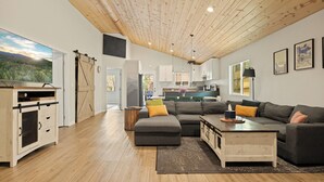 A modern living room with a wooden ceiling, a large sectional sofa, a coffee table, and a sliding barn door. - 3bdr Modern Family House - Spa, Playroom, Walkable, Pet-friendly (Big Bear Lake)