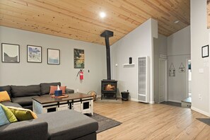 A living room with a fireplace, a sofa, a coffee table, and a wooden ceiling. - 3bdr Modern Family House - Spa, Playroom, Walkable, Pet-friendly (Big Bear Lake)