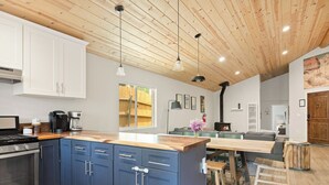 A modern kitchen with blue cabinets, a wooden ceiling, and a dining area with a table and chairs. - 3bdr Modern Family House - Spa, Playroom, Walkable, Pet-friendly (Big Bear Lake)