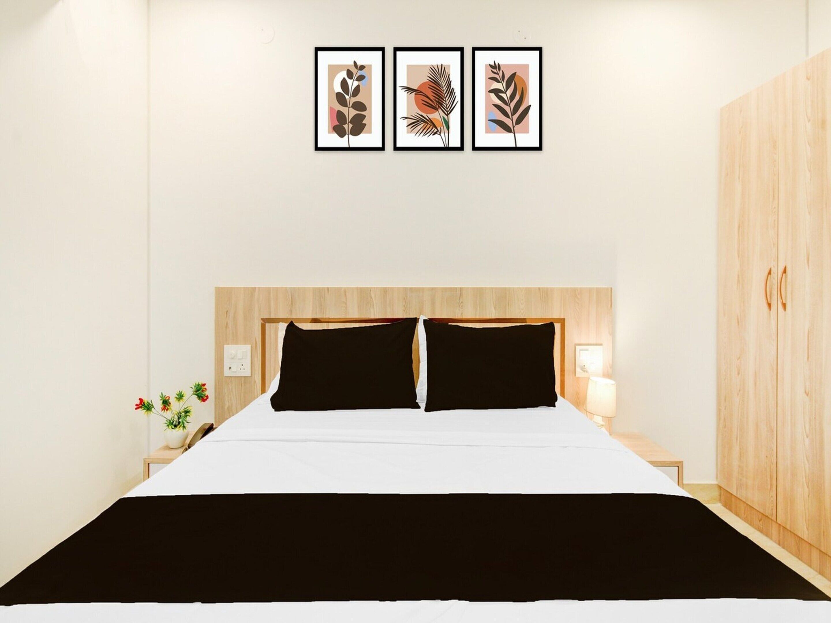 A bedroom with a wooden headboard, a bed with black and white bedding, two bedside lamps, and three framed artworks on the wall.