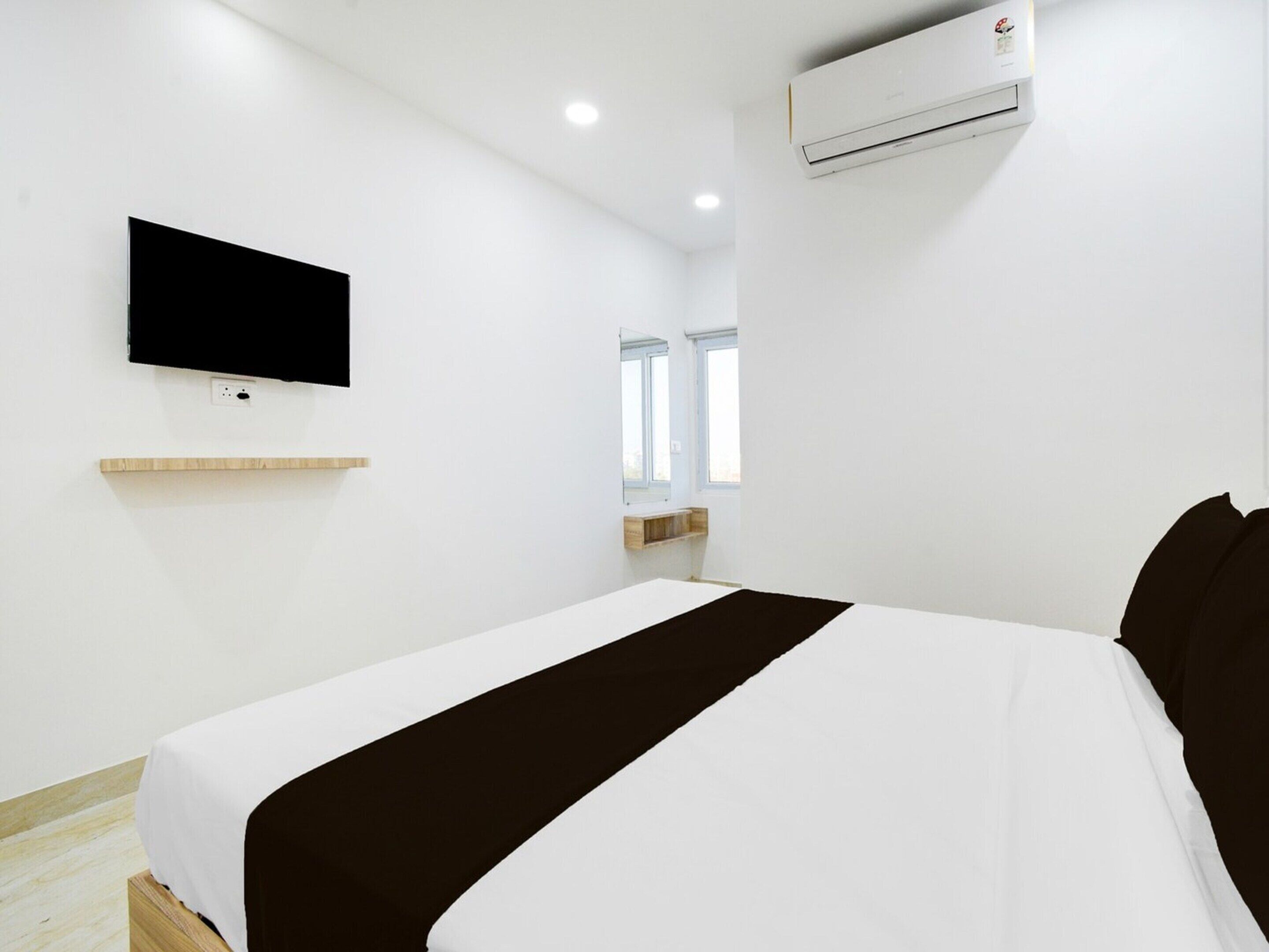 A hotel room with a bed, a mounted TV, an air conditioning unit, and a window.