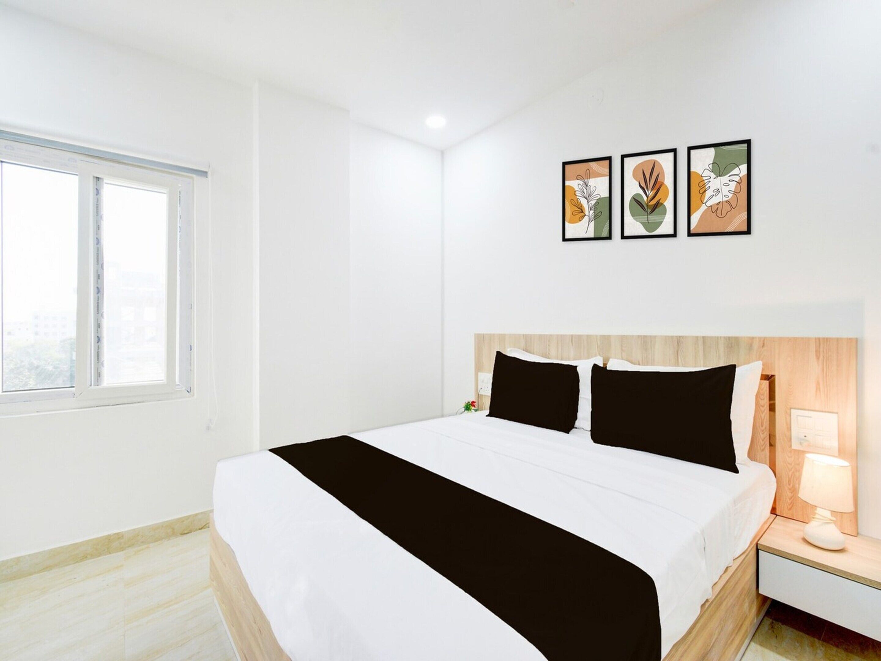 A hotel room with a bed, a nightstand, a lamp, and three wall-mounted artworks.