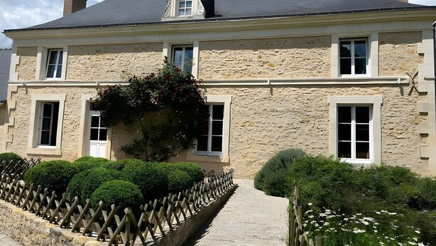 A stone building with a central entrance, multiple windows, and a small garden area with a wooden fence. - Bed and Breakfast 'La Suite Tilleul' with Shared Terrace, Shared Garden and Wi-Fi (Baugé-en-Anjou)