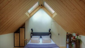 A bedroom with a sloped ceiling, a bed with pillows, a nightstand, a wardrobe, and a bookshelf. - Bed and Breakfast 'La Suite Étoilée' with Shared Terrace, Shared Garden and Air Conditioning (Baugé-en-Anjou)