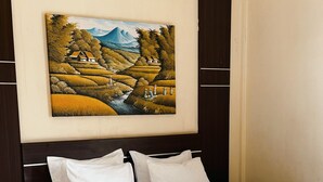Ein ordentlich bezogenes Bett mit weißen Leinentüchern und einem dekorativen Handtuch, ein dunkles Holz-Kopfteil sowie ein gerahmtes Landschaftsbild darüber.