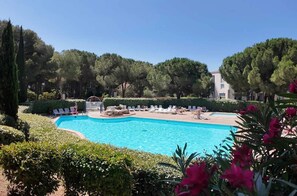 A swimming pool with lounge chairs, surrounded by trees and hedges.